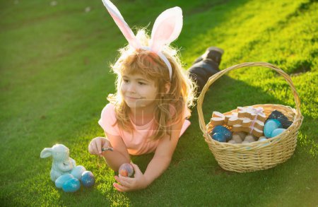 Foto de Niño con huevos de Pascua y orejas de conejo al aire libre. Chico gracioso, conejito de Pascua. Lindo niño teniendo feliz Pascua en el parque - Imagen libre de derechos