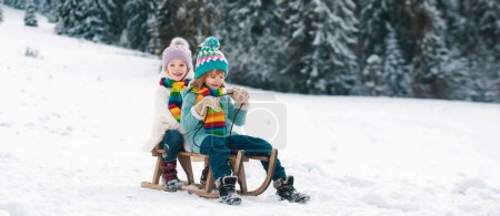 Téléchargez les photos : Amis enfants garçon et fille luge en hiver. Enfants frères et sœurs chevauchant sur des glissades de neige en hiver. Fils et fille profitent d'une promenade en traîneau - en image libre de droit