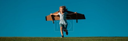 Téléchargez les photos : Bannière avec portrait d'enfants de printemps. Voyageur enfant avec des ailes de sac à dos. Enfant jouant pilote aviateur et rêve à l'extérieur dans le parc. Jeune garçon pilote contre un ciel bleu - en image libre de droit
