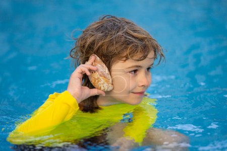 Foto de Un chico escuchando el océano en una concha. Un niño sosteniendo una concha cerca de su oreja. Feliz niño jugando en el mar. El chico se divierte al aire libre. Vacaciones de verano y concepto de estilo de vida saludable - Imagen libre de derechos
