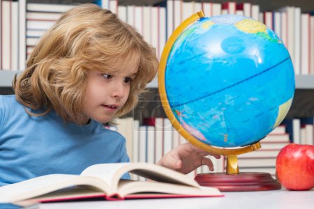 Foto de School kid looking at globe in library at the elementary school. Child from elementary school. Pupil go study. Clever schoolboy learning. Kids study, knowledge and education concept - Imagen libre de derechos