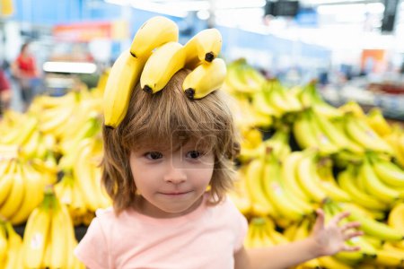 Photo for Shopping, discount, sale concept. Funny kid boy with banana on head. Child at store. Supermarket and grocery shop concept. Little child customers buying products at supermarket - Royalty Free Image