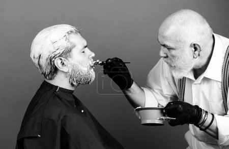 Téléchargez les photos : Homme styliste avec teinture capillaire et brosse à colorier les cheveux au salon. Processus d'un gars ayant les cheveux teints chez le coiffeur - en image libre de droit