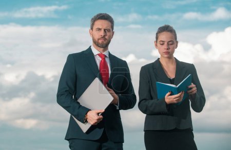 Photo for Successful business couple. Businessman and businesswomen. Successful business people standing over blue sky. Man hold laptop woman with notebook - Royalty Free Image