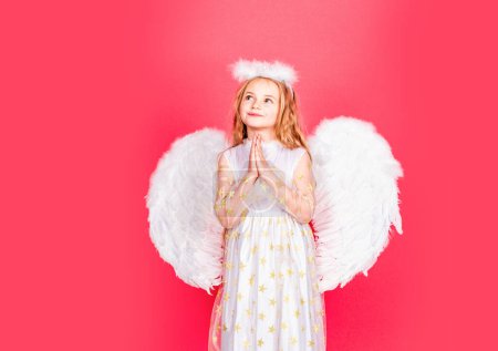 Téléchargez les photos : Enfant ange prière. Enfant à caractère angélique. Petite fille portant costume d'ange robe blanche et ailes de plumes. Consept d'enfant innocent - en image libre de droit