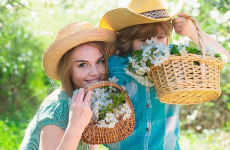 Photo for Cheerful family sniff flower basket in park. Mother with son together in garden - Royalty Free Image