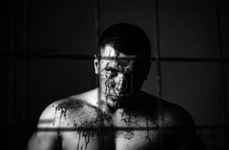 Photo for Halloween concept. Aggressive person. Strong aggressive monster behind grid. Bodybuilder nude torso soiled blood. Prison for monster. Psycho mad man. Psychic disease. Murderer brutal aggressive guy. - Royalty Free Image