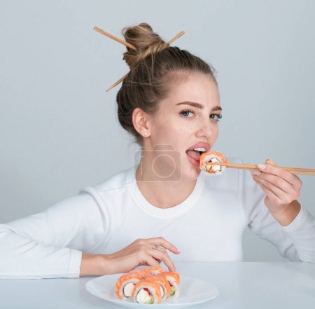 Téléchargez les photos : Sexy woman eat japanese traditional food sushi rolls. Girl is holding japanese sushi piece of roll philadelphia by chopsticks. Advert for sushi delivery of restaurants cafe - en image libre de droit