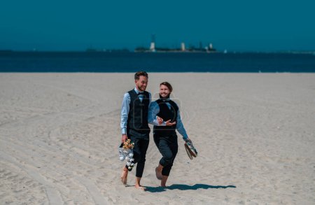 Téléchargez les photos : Des hommes gays marchant sur une plage. couple de mariage gay Lgbt ayant moment romantique ensemble après la cérémonie de mariage. Concept de LGBTQ. Mariage en couple gay. Mariage gay - en image libre de droit
