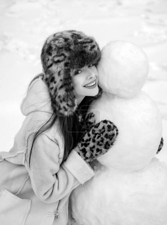Téléchargez les photos : Fille d'hiver faisant bonhomme de neige. Fille heureuse jouant avec un bonhomme de neige sur une promenade hivernale enneigée. Émotion hivernale. Jeune femme portrait d'hiver - en image libre de droit