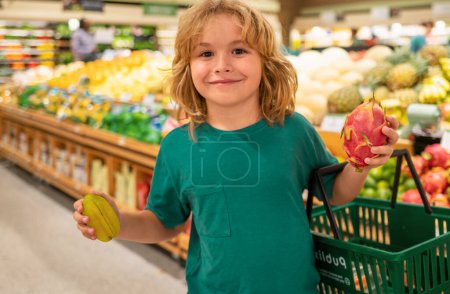 Téléchargez les photos : Enfant avec des fruits. Enfant choisissant des fruits et légumes pendant les achats au supermarché de légumes. Un gamin qui va faire du shopping. Aliments sains pour enfants - en image libre de droit