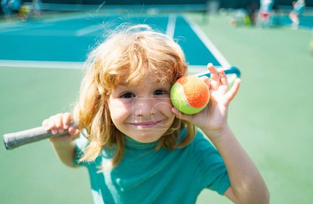Foto de Niño lindo con raqueta de tenis en la cancha en la competencia de tenis. Cara divertida de los niños - Imagen libre de derechos