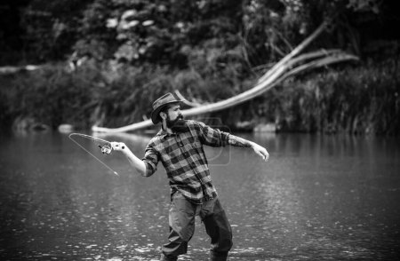 Téléchargez les photos : Beau pêcheur avec un chapeau. La pêche exige d'être attentif et pleinement présent dans le moment. Pêcheur joyeux pêchant dans une rivière à l'extérieur. Pêche lac d'eau douce étang rivière - en image libre de droit