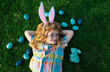 Photo for Portrait of bunny boy on Easter day. Top view of child boy hunting eggs in garden, spring family holidays. Easter bunny kids hunt easter eggs. Funny child face wear bunny ears - Royalty Free Image