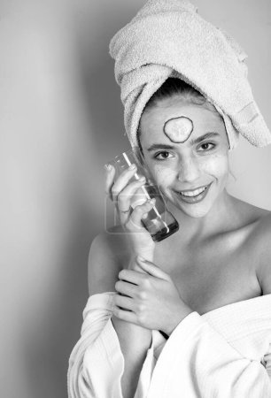 Photo for Happy smiling fresh looking young woman with a towel at her head and clay mud musk with cucumber do spa procedures. Daily skin care routine concept - Royalty Free Image