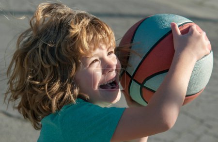 Téléchargez les photos : Mignon sourire excité garçon joue au basket-ball. Enfant drôle visage gros plan - en image libre de droit
