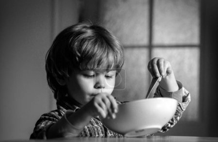 Foto de Comer niños. Un niño desayunando en la cocina. Lindo niño desayunando en casa. Bebé comiendo - Imagen libre de derechos