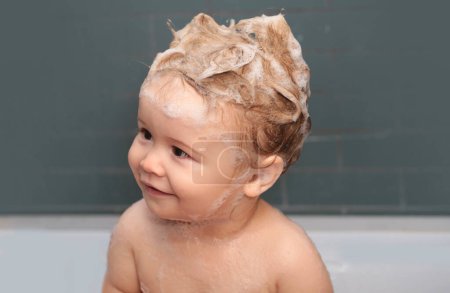 Téléchargez les photos : Bains de bébé heureux drôles dans la baignoire avec de l'eau et de la mousse. Hygiène des enfants. Les enfants drôles font face de près - en image libre de droit