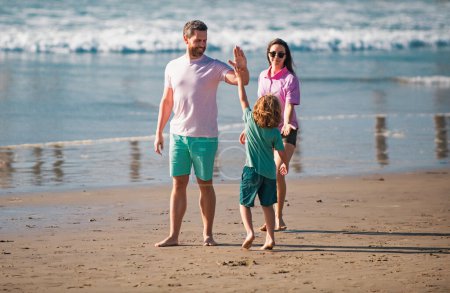 Téléchargez les photos : Promenade familiale le long de la plage. Parents heureux avec enfant jouant sur la plage. Passer l'été dans la nature - en image libre de droit