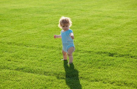 Téléchargez les photos : Adorable petit garçon à l'extérieur posant sur l'herbe verte. Enfant en bonne santé - en image libre de droit