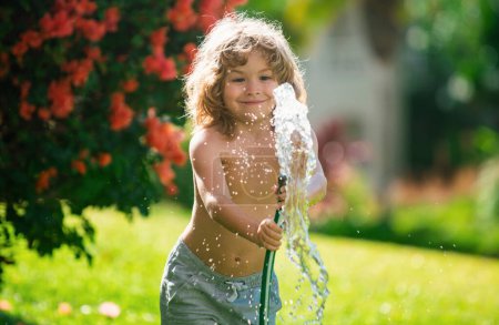Foto de Niño americano jugando con manguera de jardín en el patio trasero. Divertido niño emocionado divertirse con spray de agua en el fondo de la naturaleza patio. Actividades al aire libre para niños de verano - Imagen libre de derechos