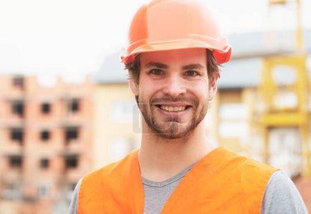 Photo for Construction worker man in work clothes and a construction helmet. Portrait of positive male builder in hardhat working at construction site - Royalty Free Image