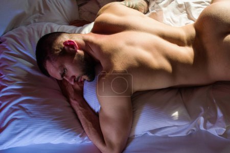 Foto de Sexy naked young man on bed. Nude male body. Sexy model laying in big bed. Young muscular male model lying back in bed with sexy body. Bare torso. Muscular male torso, bare shoulders - Imagen libre de derechos