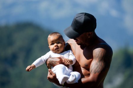 Foto de Retrato de cerca del padre afroamericano besando al bebé birracial multirracial. Padre abrazo Biracial niño al aire libre. Padre con el bebé Biracial en la naturaleza. Hathers mano llevando Biracial bebé - Imagen libre de derechos