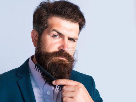 Téléchargez les photos : Jeune homme coiffant sa longue barbe avec un peigne. Homme barbu avec barbe, gay barbu. Concept de salon de coiffure. Moustache hommes - en image libre de droit