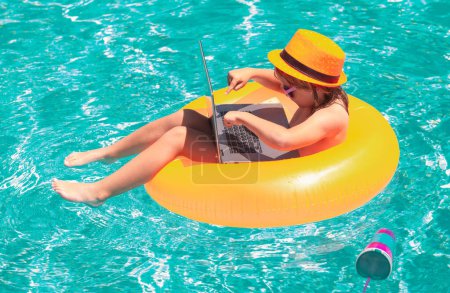 Téléchargez les photos : Travail en ligne et se détendre dans la piscine. Enfant avec ordinateur portable dans la piscine en journée d'été - en image libre de droit
