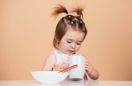 Photo for Cute funny babies eating, baby food, Babys first meal. The child eats on his own with a cup - Royalty Free Image