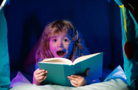 Foto de Muchacho excitado con libro. Niños, hora de dormir. Niño leyendo un libro en la cama - Imagen libre de derechos