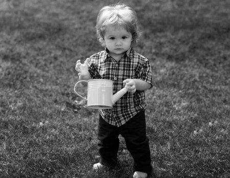 Téléchargez les photos : Mignon petit garçon enfant arrosage fleurs avec arrosoir. Lifestyle portrait bébé enfant en happines à l'extérieur dans la prairie - en image libre de droit