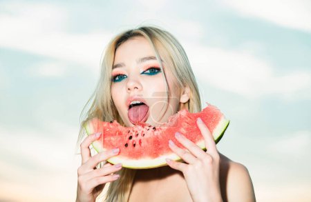 Téléchargez les photos : Fruit tropical estival sexy. Sensuelle jeune femme lécher pastèque avec la langue sexy. Goût d'été. Joyeux jeune femme tenant tranche de pastèque contre la moitié de son visage et lécher la pastèque - en image libre de droit