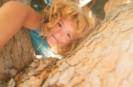Photo for Happy child playing in the garden climbing on the tree. Funny kids face - Royalty Free Image