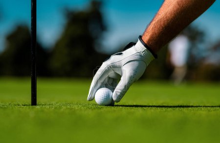 Téléchargez les photos : Homme golfeur avec gant de golf. Joueur de golf jouant au golf par temps ensoleillé. Main mettant balle de golf sur tee - en image libre de droit