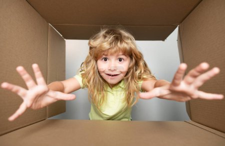 Photo for Funny child boy is opening gift and looking inside cardboard box. Child with open box take by hand gift - Royalty Free Image