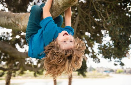 Téléchargez les photos : Loisirs d'enfance. Enfants heureux suspendus à l'envers sur l'arbre et s'amuser dans le parc d'été. Monkeying autour - en image libre de droit