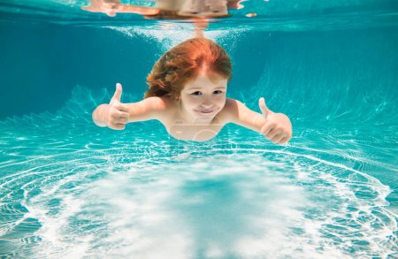 Foto de Los niños nadan bajo el agua en la piscina. Niño nadando bajo el agua con los pulgares arriba - Imagen libre de derechos