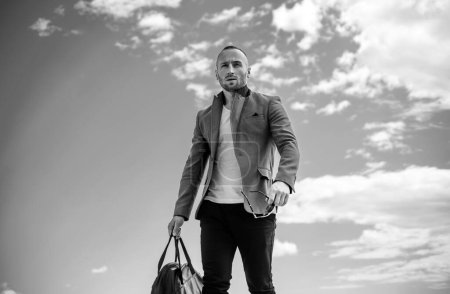 Téléchargez les photos : Portrait de jeune homme élégant avec sac dans la rue, style de vie. Jeune homme de la mode extérieur regardant loin - en image libre de droit