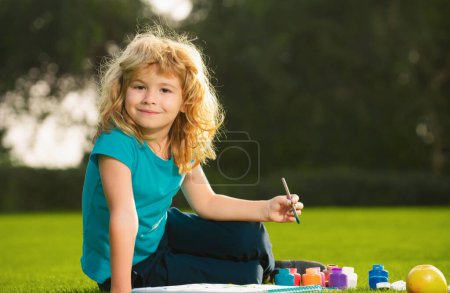 Téléchargez les photos : Enfant garçon peinture dans la nature printanière. Des écoliers dessinent dans un parc d'été, peignent de l'art. Petit peintre dessiner des images en plein air - en image libre de droit