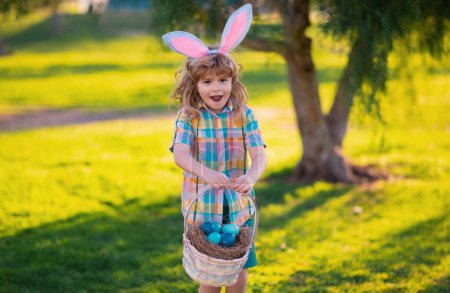 Foto de Niña conejita. Niño cazando huevos de Pascua, poniendo en la hierba. Niño en conejo orejas de conejo al aire libre. Conejito de Pascua niños - Imagen libre de derechos
