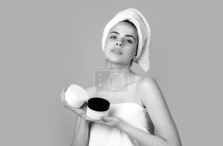 Téléchargez les photos : Crème cosmétique sur visage de femme avec bouteille de crème. Soins du corps. Femme avec serviette appliquer la crème sur la peau. Des gestes pour la publicité. Fond beige - en image libre de droit