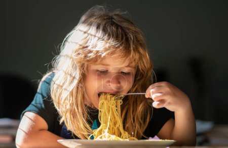 Photo for Little kid eating spaghetti in kitchen. Child eating on blurred background. Hungry little boy eating. Home food for kids - Royalty Free Image