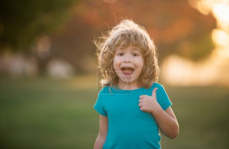 Foto de Portrait of a happy laughing child summer outdoor. Close up positive kids face. Thumbs up. Amazed surprised excited kids emotions. - Imagen libre de derechos