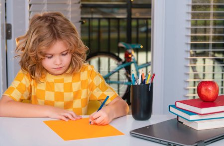 Téléchargez les photos : Un écolier qui étudie l'écriture à la maison. Un gamin de l'école primaire. Enfant élève faisant ses devoirs dans sa chambre - en image libre de droit