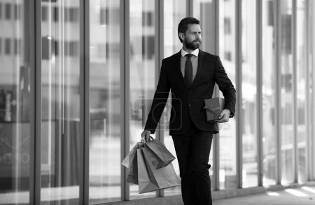 Téléchargez les photos : Homme d'affaires faisant du shopping en ville. bel homme en costume avec des sacs à provisions - en image libre de droit