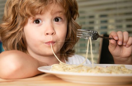 Téléchargez les photos : Enfant drôle manger des pâtes, des spaghettis, le visage de près. Portrait tête d'enfant - en image libre de droit