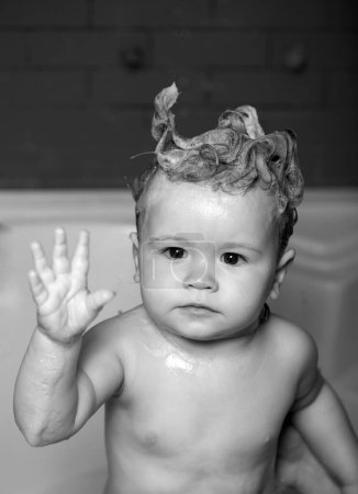 Téléchargez les photos : Laver adorable bébé dans la salle de bain. Enfant avec de la mousse de savon sur les cheveux prenant un bain. Portrait rapproché d'un enfant souriant, des soins de santé et de l'hygiène des enfants. - en image libre de droit