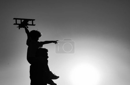 Photo for Sunset silhouette of Father carrying his son on shoulders. Child son pilot and dad daddy father with airplane - Royalty Free Image